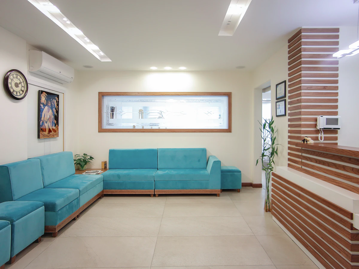 Recepção da clínica com sofá azul-turquesa, planta e balcão de madeira